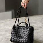 Model holding black woven leather tote bag with gold rope accent and double strap