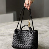 Model holding black woven leather tote bag with gold rope accent and double strap