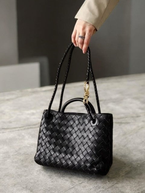 Model holding black woven leather tote bag with gold rope accent and double strap